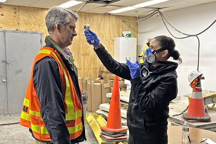 A woman holds a thermometer sensor to a construction worker as part of the MTA's “Temperature Brigade” consisting of medically trained personnel to check temperatures of heroic employees at 22 strategic locations, including at the East End Gateway project in Penn Station.